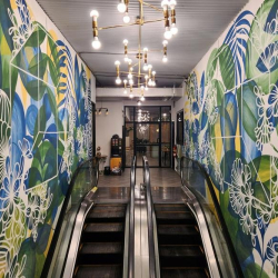 Escalator entryway flanked by vibrant tropical murals and modern light fixtures.