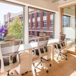 Bright, sunlit office area with white desks, ergonomic chairs, and floor-to-ceiling city views.