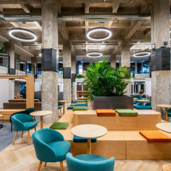 Wide open-plan workspace with long wooden tables and exposed industrial beams.