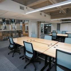 Bright open-plan office with individuals working at communal wooden desks.