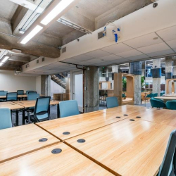 Open-plan workspace with light wood desks and industrial concrete ceilings.
