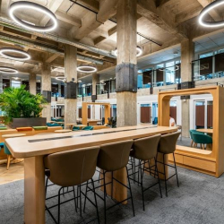 Coworking area with high-top tables and blue chairs near street-facing windows.