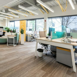 Bright open-plan coworking area with rows of desks and large windows.