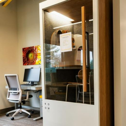 Small glass work pod equipped with a desk, chair, and computer monitor.