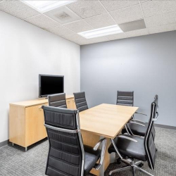 Professional meeting room with a wooden table, black chairs, and a media screen.