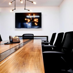 Sleek conference room at Kenex Plaza with a long wooden table and wall-mounted screen.. Click for details.