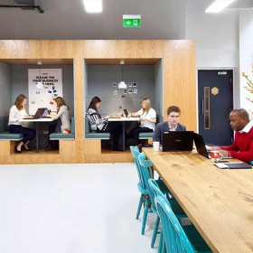 Modern coworking space at Plaza 2000 featuring private wooden booths and a long communal table.. Click for details.